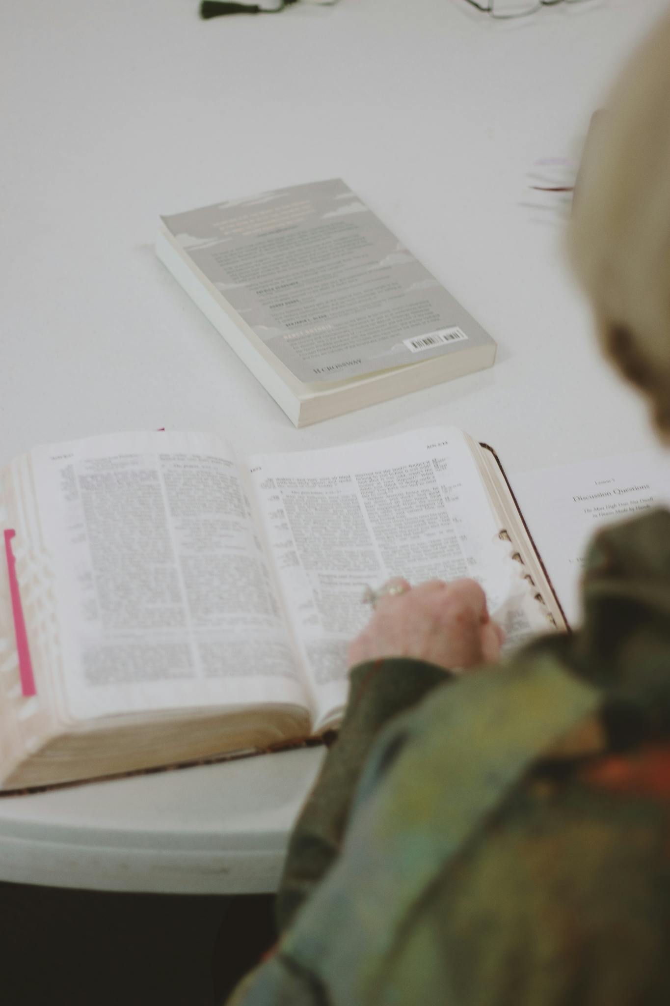 An elderly woman studying the Bible at a table, focused on scripture.